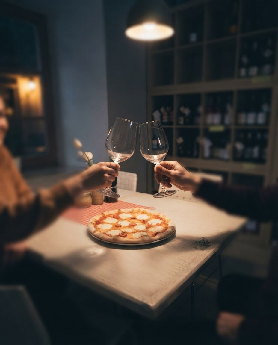Dva hosté si připíjejí u stolu s pizzou